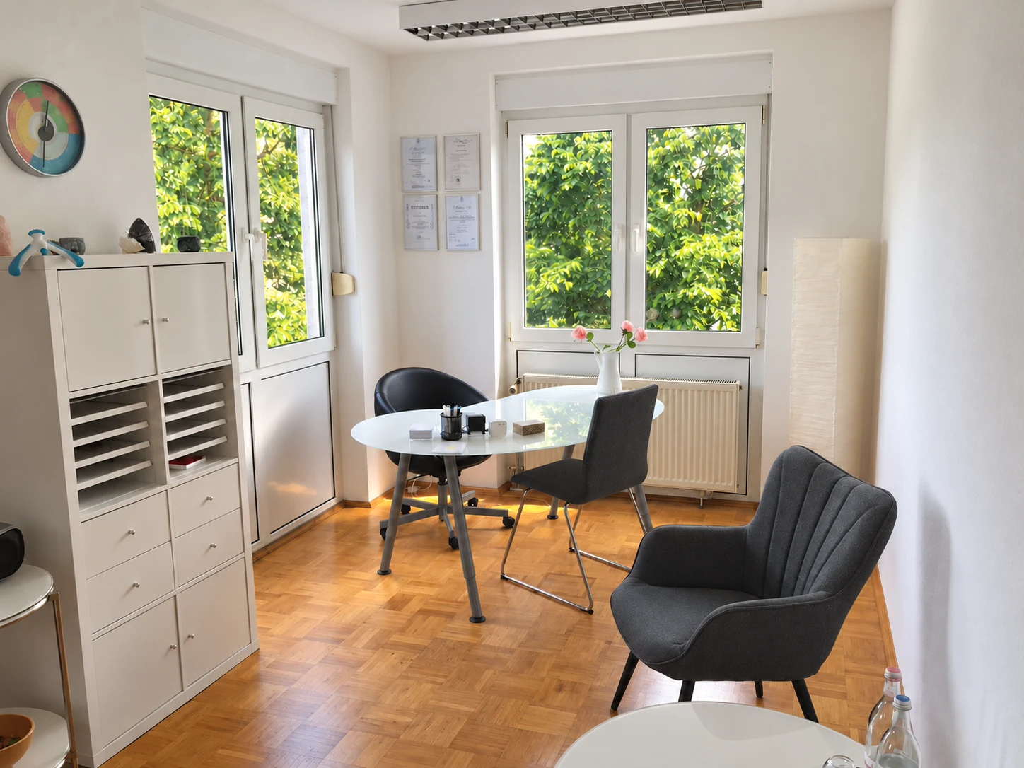 Praxisraum mit Sitzgelegenheiten, Glastisch und Fenstern
